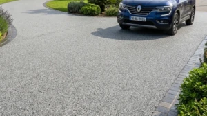 Zoom sur gravier d'une allée carrossable en résine avec voiture bleu et jardin entourant l'allée.